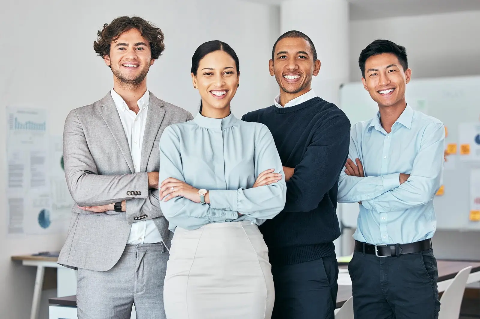 A team of Graphic designer and video animators that are Three men and one woman with black hair and bright skin tone are standing together, smiling with folded arms, looking towards the camera.